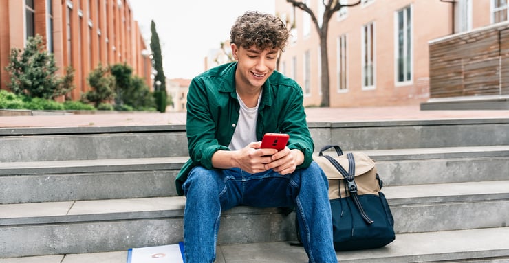 college-student-smiling-at-phone-messaging-druid-ai-admissions-agent-on-campus-steps