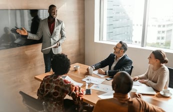 Person pointing to a screen and showing something to colleagues in a formal office setting